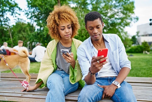 young couple sitting in the park and using their cellphones 