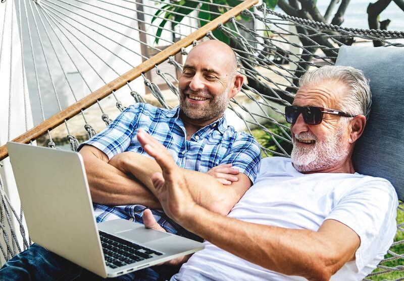 Two older gay men happily using a laptop together.